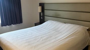A neatly made bed with a headboard, a bedside table with a lamp, and a window with curtains.