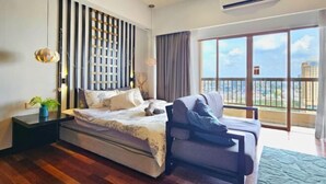A modern bedroom with a bed, a sofa, a nightstand, a decorative wall panel, and a large window with a balcony view. - Sunway Studio Homestay 1-min walk Sunway Pyramid Mall & Lagoon by Cloud Host (Subang Jaya)