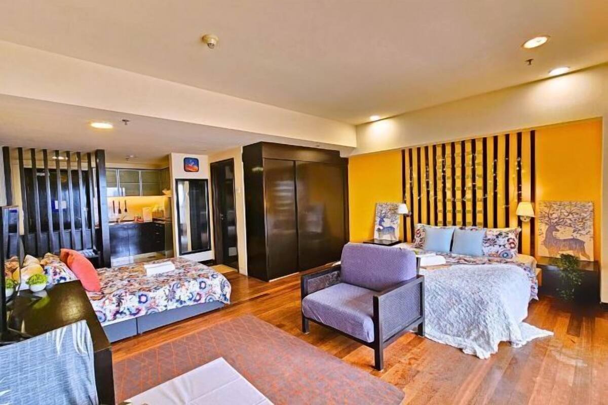 A modern hotel room with a sofa, a chair, a bed, and a large mirror.