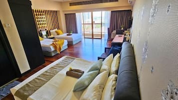 A hotel room with a large bed, a sofa, a desk, and a balcony with curtains.