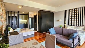 A modern living room with a sofa, a dining table, and a kitchen area in the background. - Sunway Studio Homestay 1-min walk Sunway Pyramid Mall & Lagoon by Cloud Host (Subang Jaya)