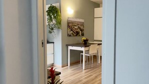 Een gang die leidt naar een eetgedeelte met een tafel, stoelen, een plant in pot en een vloerkleed.