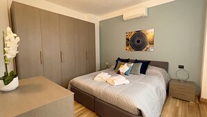 Een moderne slaapkamer met een groot bed, een kledingkast, een nachtkastje en een decoratief wandobject.