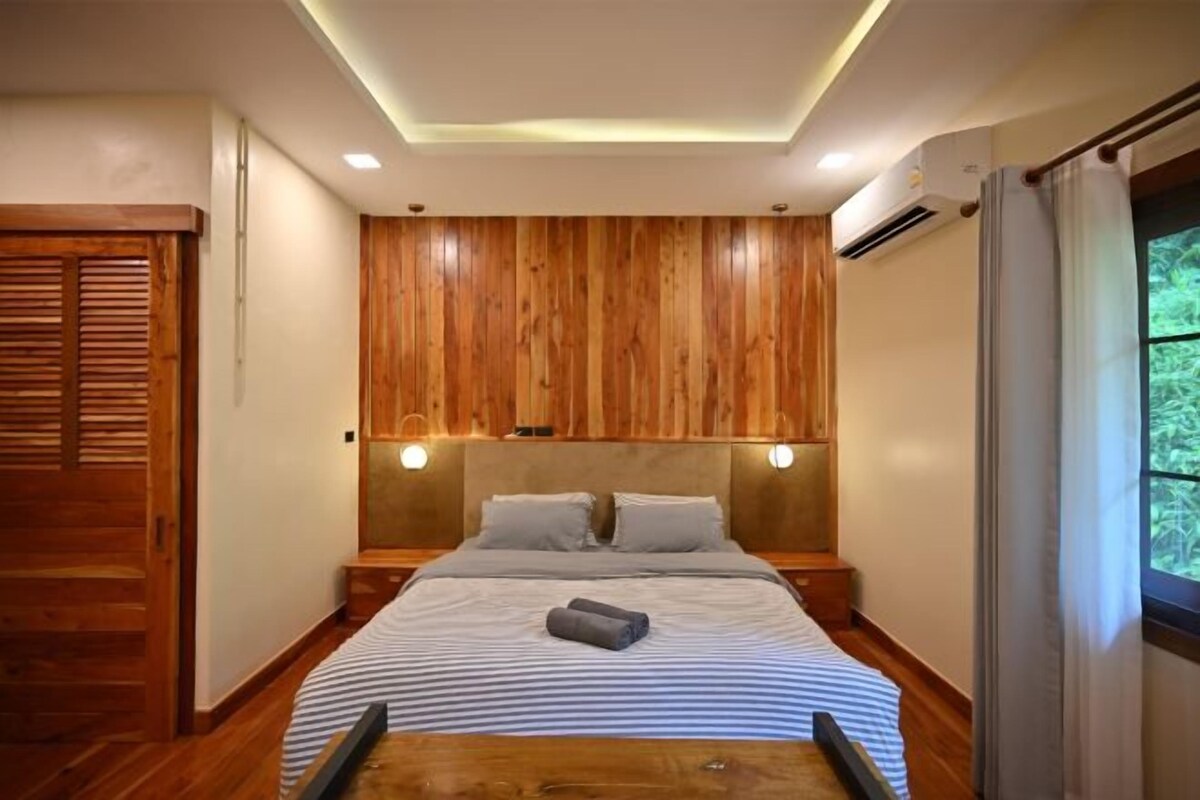Un dormitorio con cabecera de madera, una cama con ropa de cama a rayas y una mesita de noche con una lámpara.