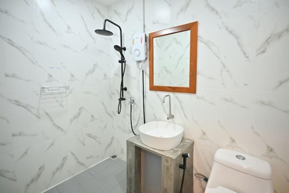 Un baño con pared de mármol, espejo con marco de madera, lavabo blanco y retrete.
