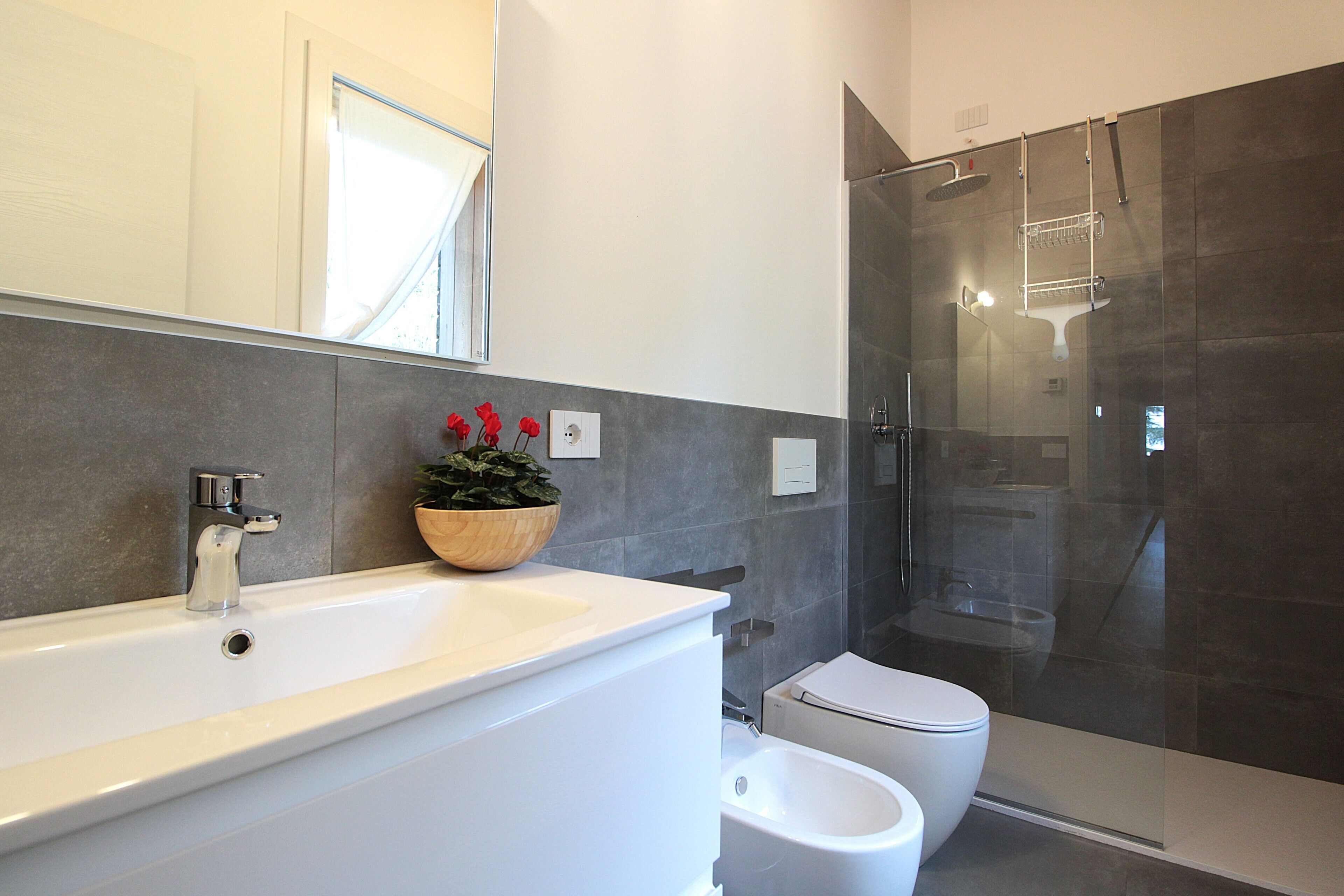 A modern bathroom with a large white sink, a glass-enclosed shower, and a toilet.