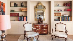 A room with two ornate chairs, a large mirror, and bookshelves filled with books and decorative items. - AN ICONIC SPACE  IN AN ICONIC LOCATION  - AVENUE RAPP – NEXT TO EIFFEL   (Paris)