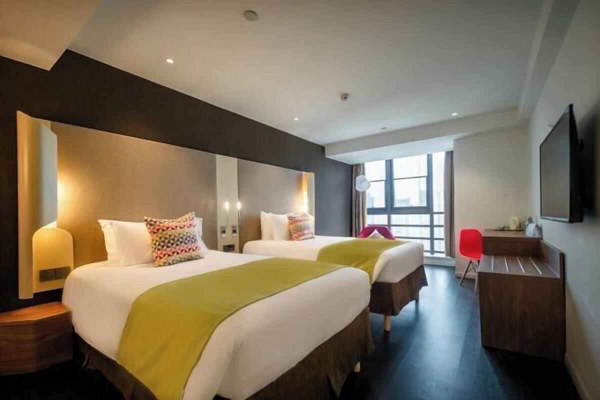 A hotel room with two beds, a desk, a chair, and a large window.