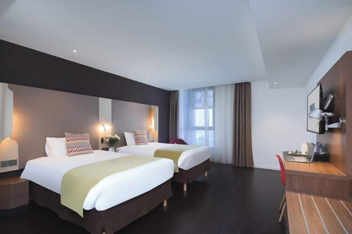 A hotel room with two beds, a desk, and a chair.