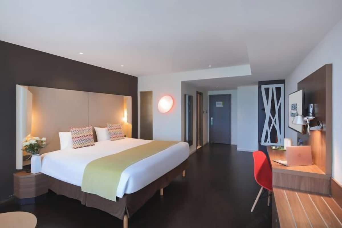 A modern hotel room with a large bed, bedside tables, a desk with a chair, and a TV.