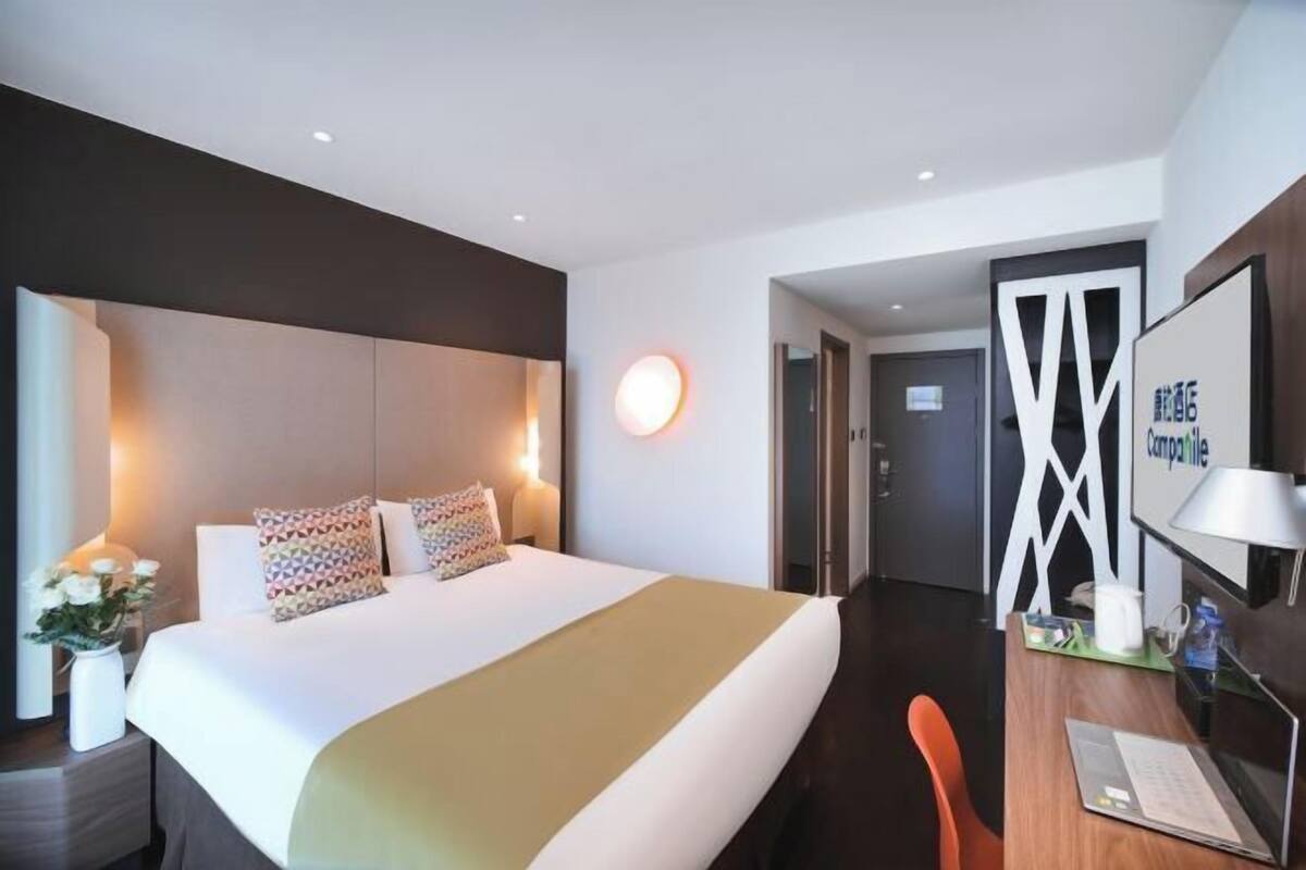 A modern hotel room with a large bed, a desk with a laptop, and a wall-mounted TV.