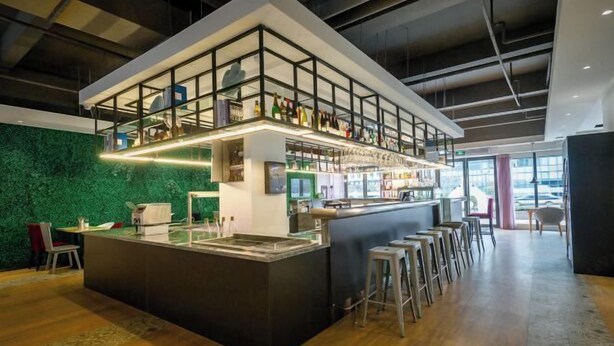 Angolo bar moderno con parete verde, bancone alto e sgabelli.