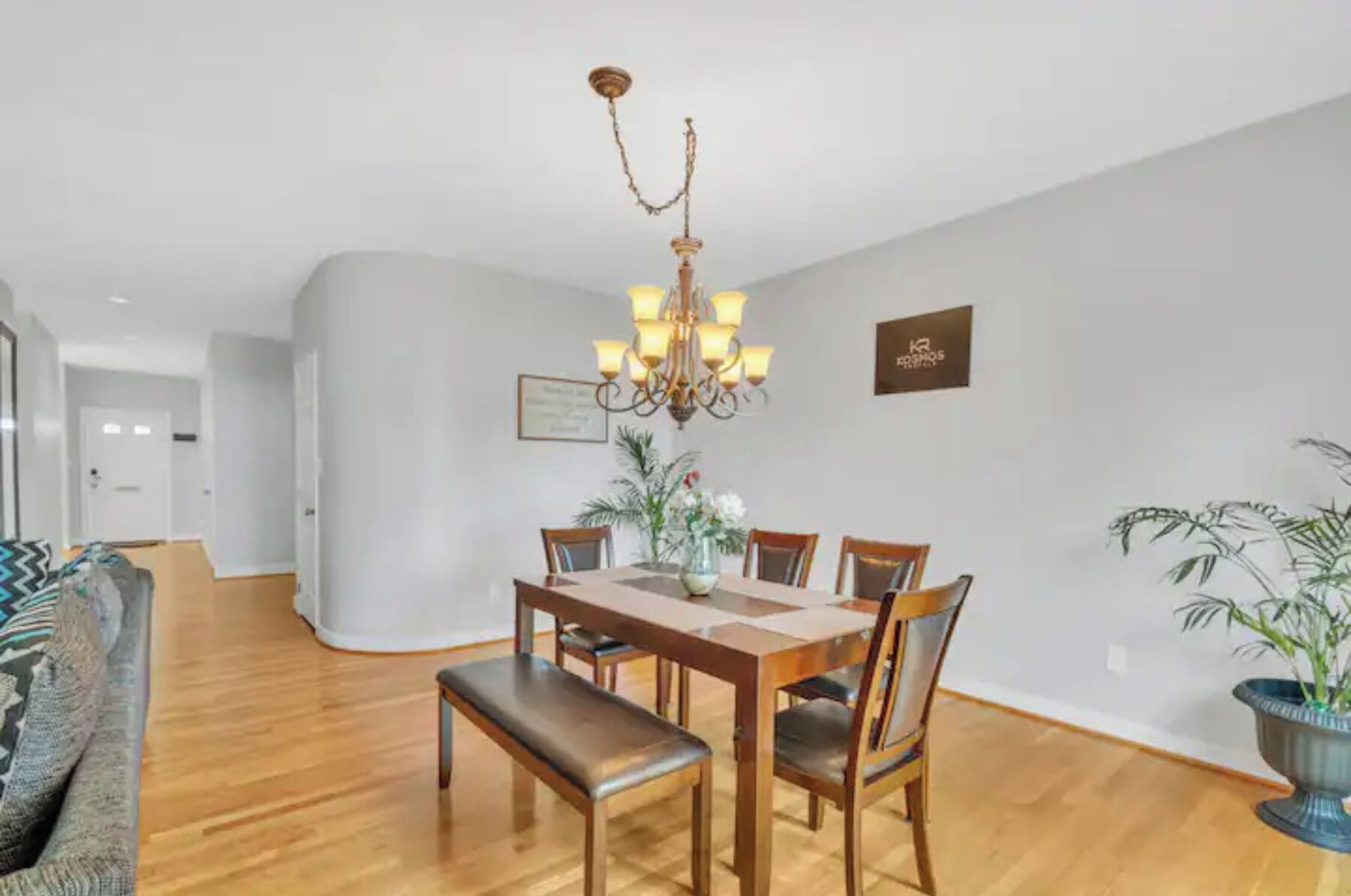 A dining area with a wooden table, chairs, a bench, and a chandelier.