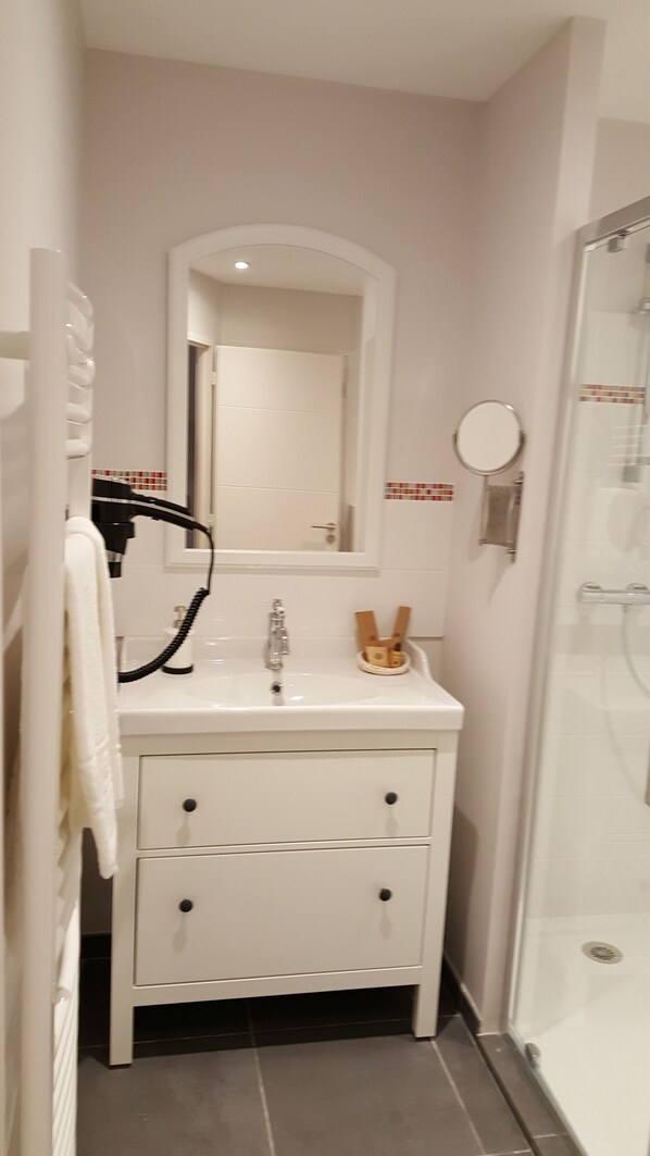 A bathroom with a white vanity, a mirror, a towel rack, and a shower area. - Hôtel Chez Jaqueline (Tours)