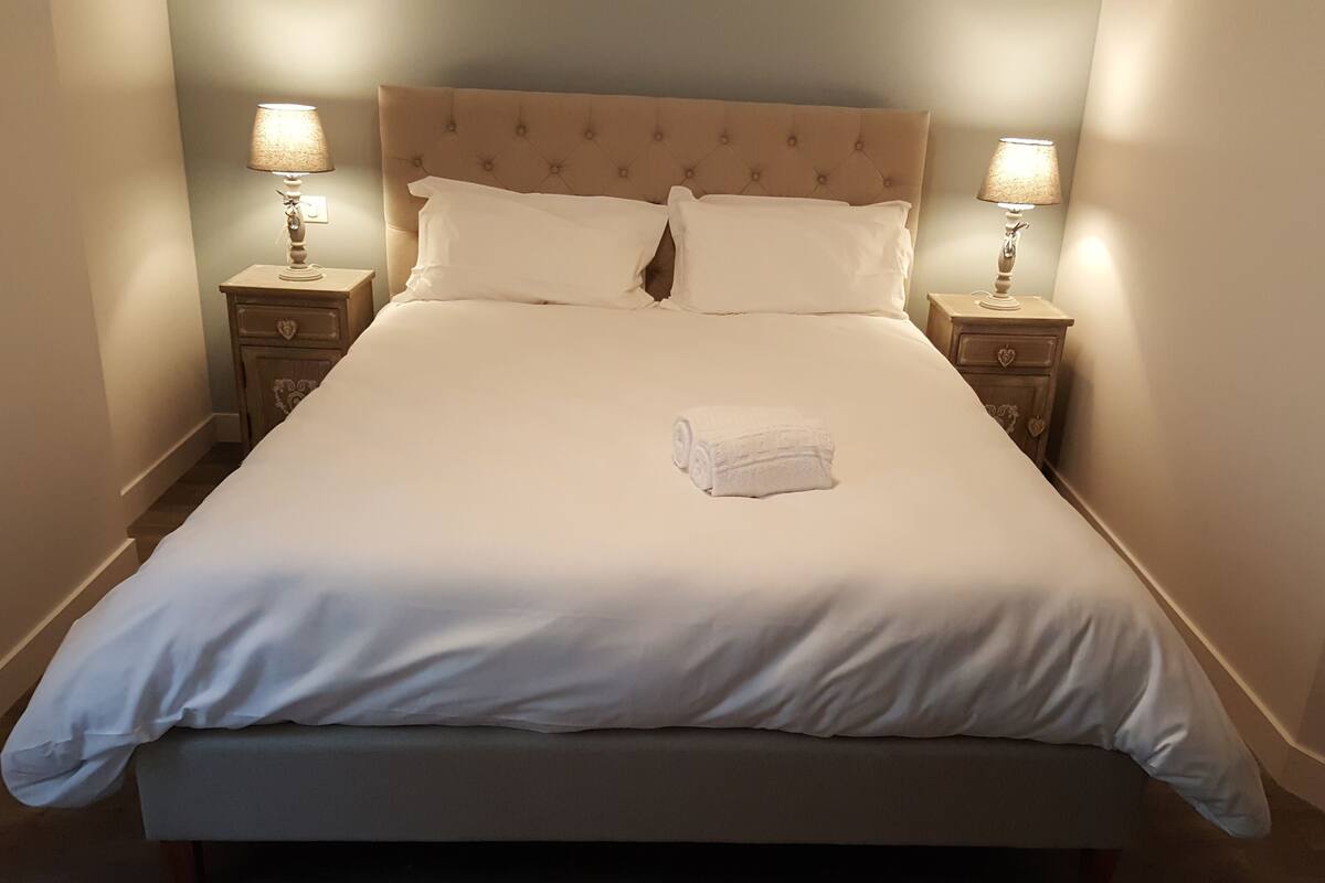 Un lit bien fait, avec une serviette blanche roulée, deux tables de chevet avec des lampes et une tête de lit capitonnée.