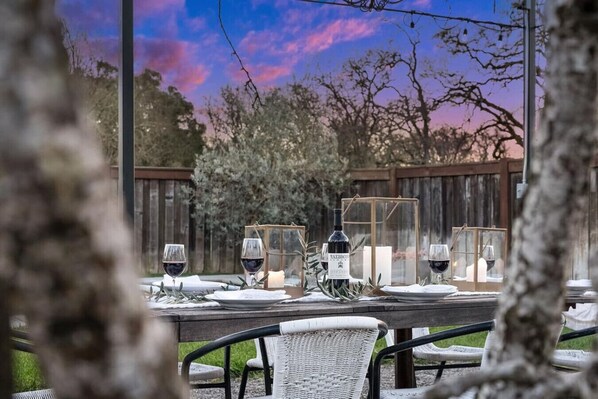 An outdoor dining area with a wooden table set for two, surrounded by wicker chairs.