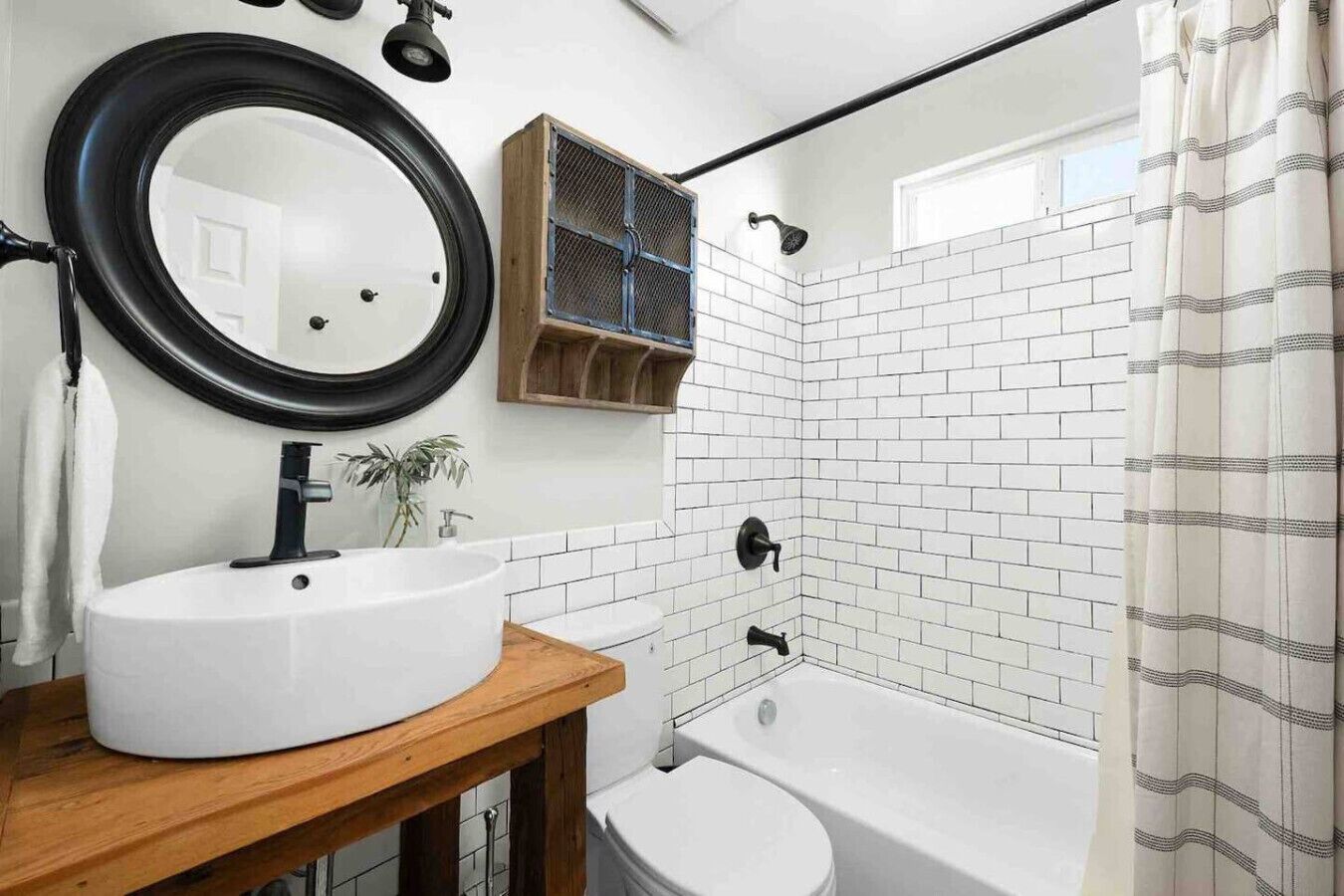 Une salle de bain moderne avec un lavabo blanc, un miroir rond, un meuble-lavabo en bois, une baignoire et un rideau de douche.