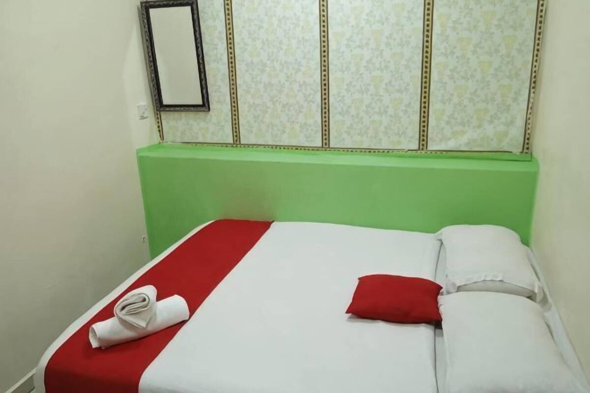 A bed with a red and white bedspread, a red pillow, and a rolled towel.
