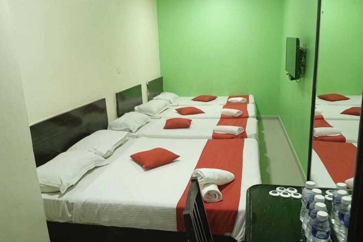 A hotel room with multiple beds, each with white linens and red pillows, a green wall, and a black headboard.