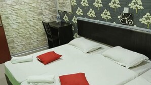 A neatly made bed with white and red pillows, a stone wall, and a floral wallpaper pattern.