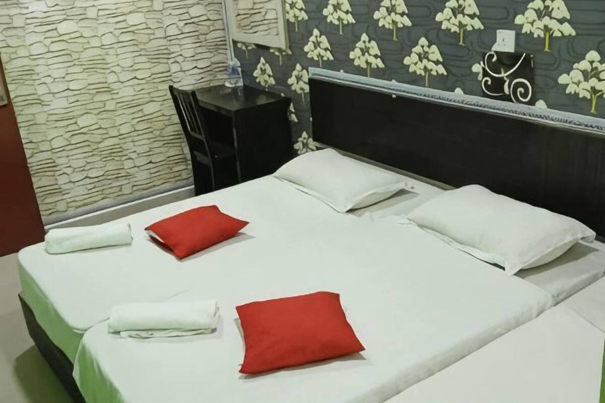 A neatly made bed with white and red pillows, a stone wall, and a floral wallpaper pattern.
