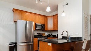 A modern kitchen with wooden cabinets, stainless steel appliances, and a central island with bar stools. - Flexhome Wicker Park • Stylish 2BR • Sleeps 6 (Chicago)