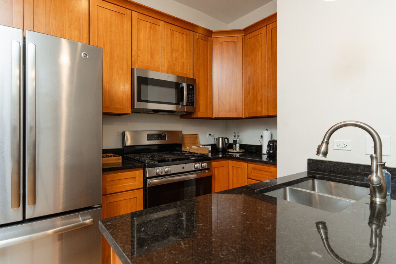 Una cocina moderna con armarios de madera, electrodomésticos de acero inoxidable, encimera de granito y pileta de acero inoxidable.