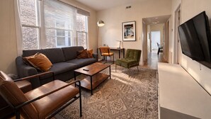 A living room with a sofa, coffee table, chairs, a TV, and a patterned rug. - Flexhome Wicker Park • Stylish 2BR • Sleeps 6 (Chicago)