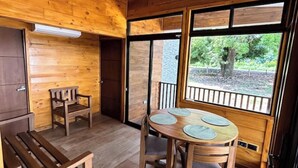 A wooden interior with a round table, benches, and large windows offering a view of greenery. - Casa Mango Lepanto #9. Charming 2-bedroom cabin AC, WiFi in enjoyable Lepanto. (Lepanto)