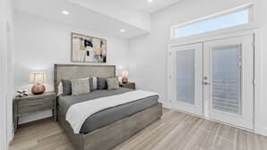 Un dormitorio moderno con una cama grande, dos mesitas de noche con lámparas, una luz en el techo y un amplio ventanal con persianas.