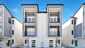 Un moderno edificio de apartamentos simétrico con balcones de dos pisos, ventanas amplias y una entrada central.