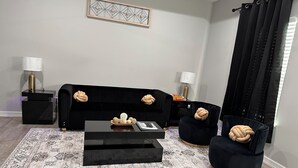 Un salon moderne avec un canapé noir, deux fauteuils, une table basse et un tapis à motifs.