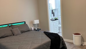 Une chambre à coucher moderne avec un grand lit, une table de chevet, une lampe et une armoire blanche.