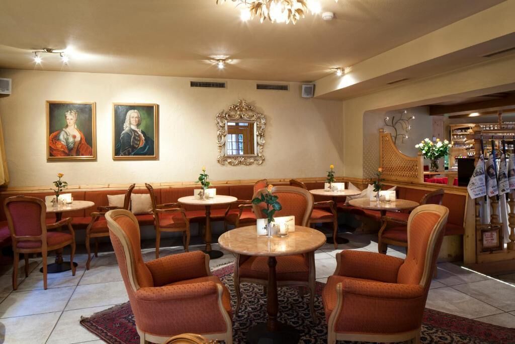 Un restaurant avec des tables rondes et des chaises recouvertes d’un tissu orange, un lustre et des tableaux accrochés aux murs.