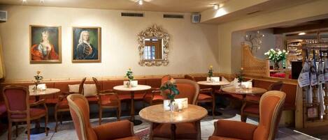 Un restaurant avec des tables rondes et des chaises recouvertes d’un tissu orange, un lustre et des tableaux accrochés aux murs.
