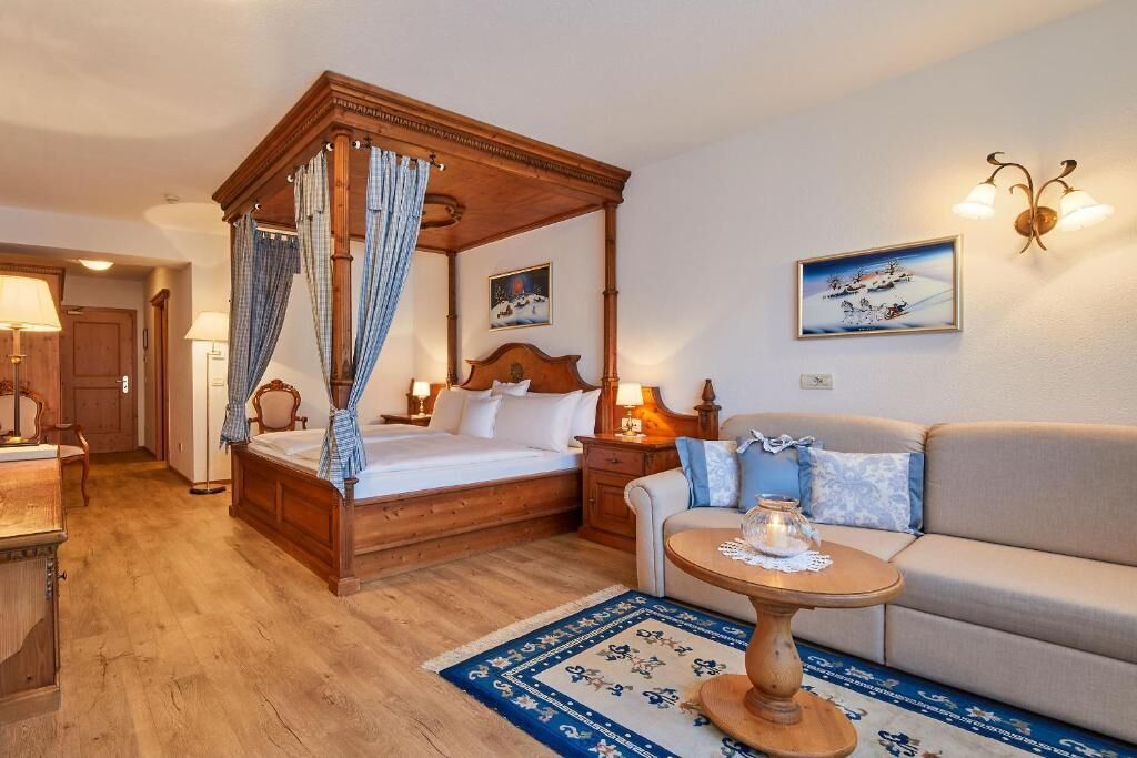 Un dormitorio con una cama con dosel, un sofá, una pequeña mesa redonda y dos lámparas fijadas a la pared.