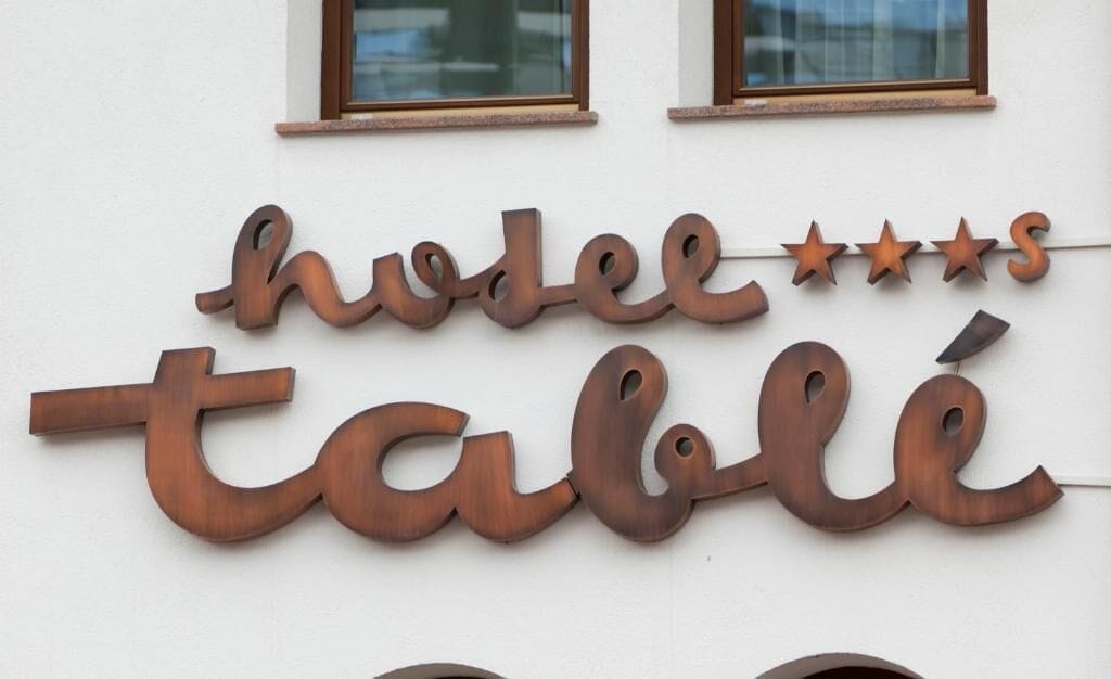 A hotel sign with the name 'hôtel table' in a rustic metal font, with three stars above the name.