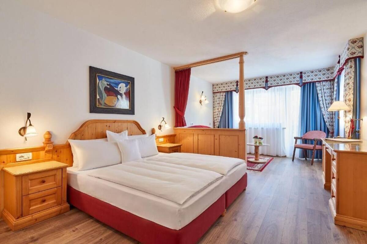 A hotel room with a large bed, wooden headboard, bedside tables, a nightstand, a desk, and a chair.