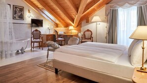 Ein Schlafzimmer mit Holzboden, einem Bett, einem Schreibtisch, zwei Stühlen, einem Fernseher und einer Badewanne.