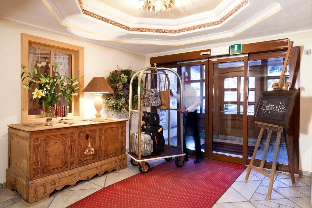 Eine Hotelhalle mit einem alten Holzschrank, einem Gepäckwagen, einem roten Teppich und einem Tafelschild.