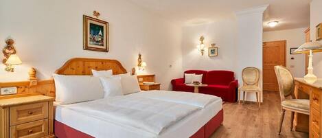 Una habitación de hotel con una cama grande, cabecero de madera, dos mesitas de noche con lámparas, un sofá rojo, una silla de madera y un aparador de madera.