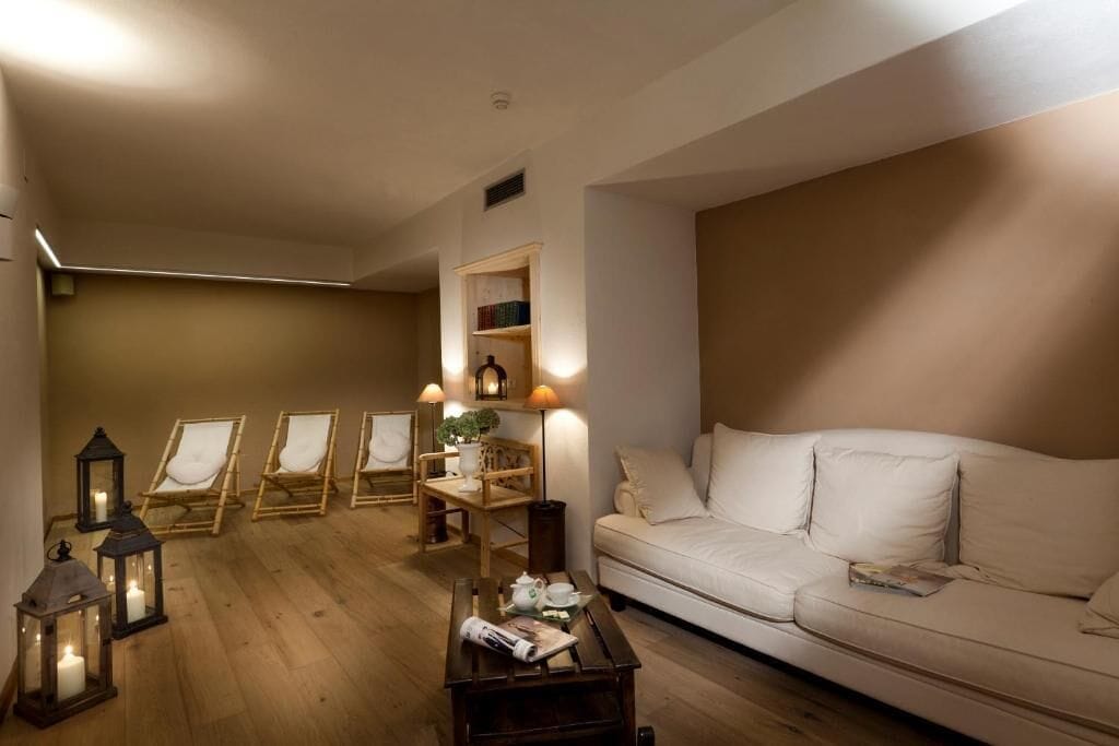 A living room with a beige sofa, four lounge chairs, a coffee table, and a bookshelf with books.