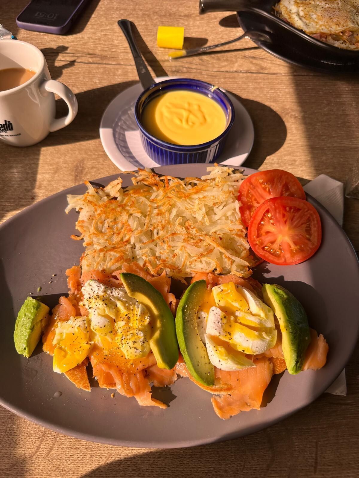 A plate with smoked salmon, avocado slices, and a tomato on a wooden table.