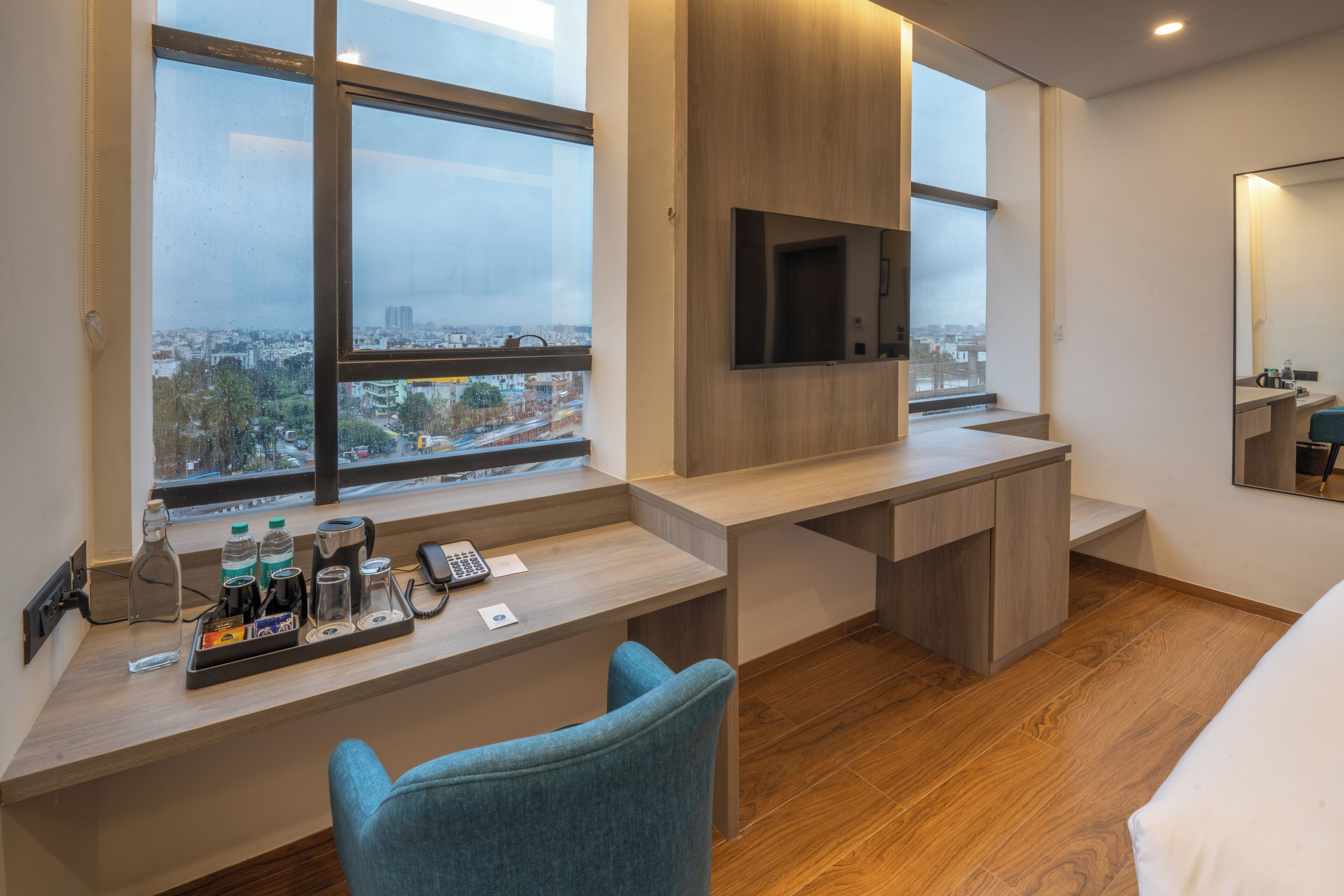 Una habitación de hotel moderna con un escritorio grande, una silla, un televisor montado en la pared y un ventanal con vistas a la ciudad.