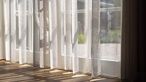 Una habitación con ventanas amplias cubiertas por cortinas traslúcidas que dejan entrar luz natural.