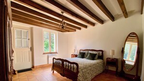 Un dormitorio con una cama de madera, un espejo grande, una ventana y una puerta.