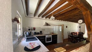Una cocina con pared de ladrillo, vigas de madera, un lavamanos, una estufa y una zona de comedor con sillas y una mesa.
