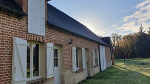 Un edificio de ladrillo con contraventanas blancas, techo de tejas y un patio con césped.