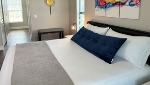 A bedroom with a bed, a bench, a wall clock, a painting, and a window with blinds.