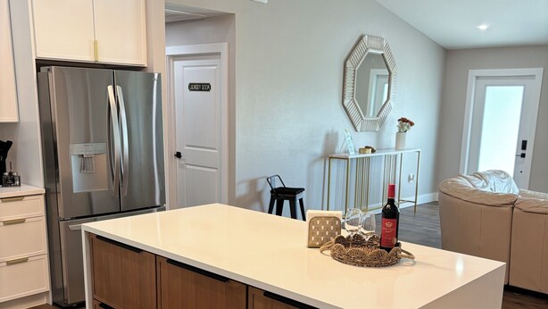 A modern kitchen with a central island, stainless steel refrigerator, and wooden cabinets.